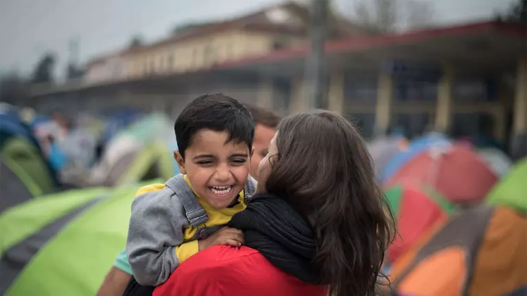 Un miembro de Save the Children sostiene en brazos a un niño sonriente